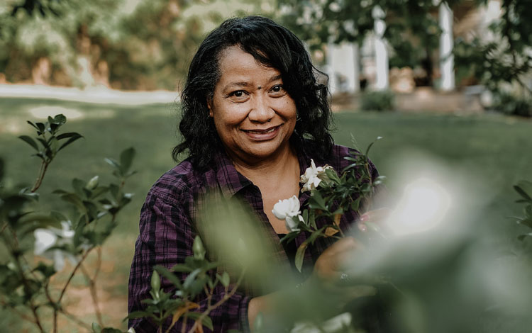 Woman peeking through a green plant, smiling with dark brown curly hair.